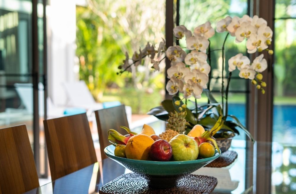 A vibrant tropical dining table with palm leaves, orchids, woven décor, and colorful fruit.