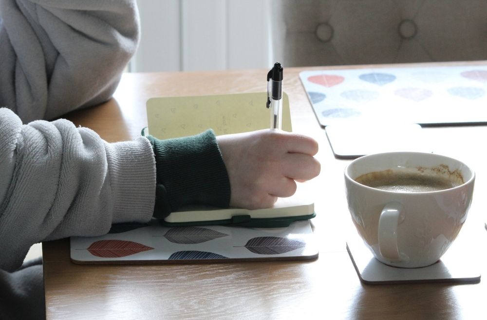 A notebook planner beside a calendar, guest list, and coffee cup, with someone making plans for an upcoming gathering.