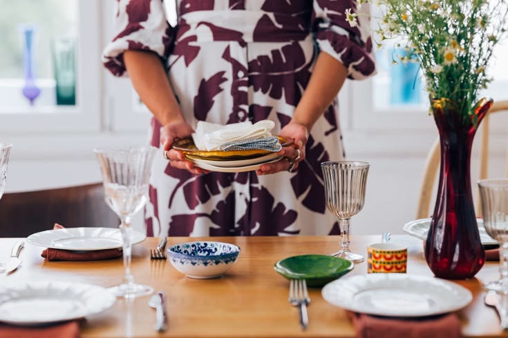 host beginning to clear dishes while guests continue a final conversation