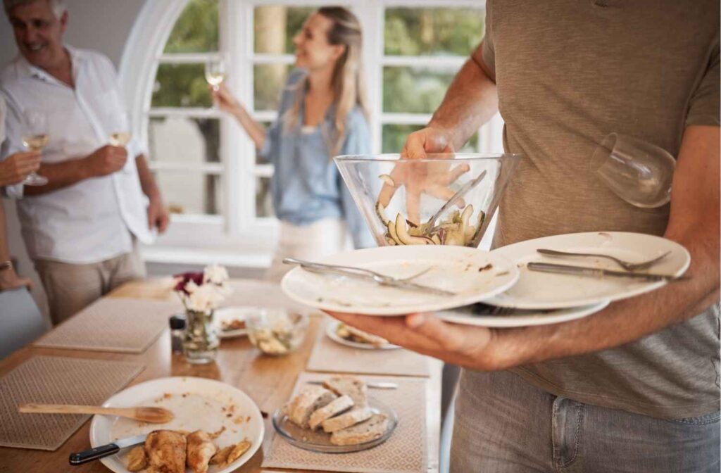 man clearing plates from dinner table after party
